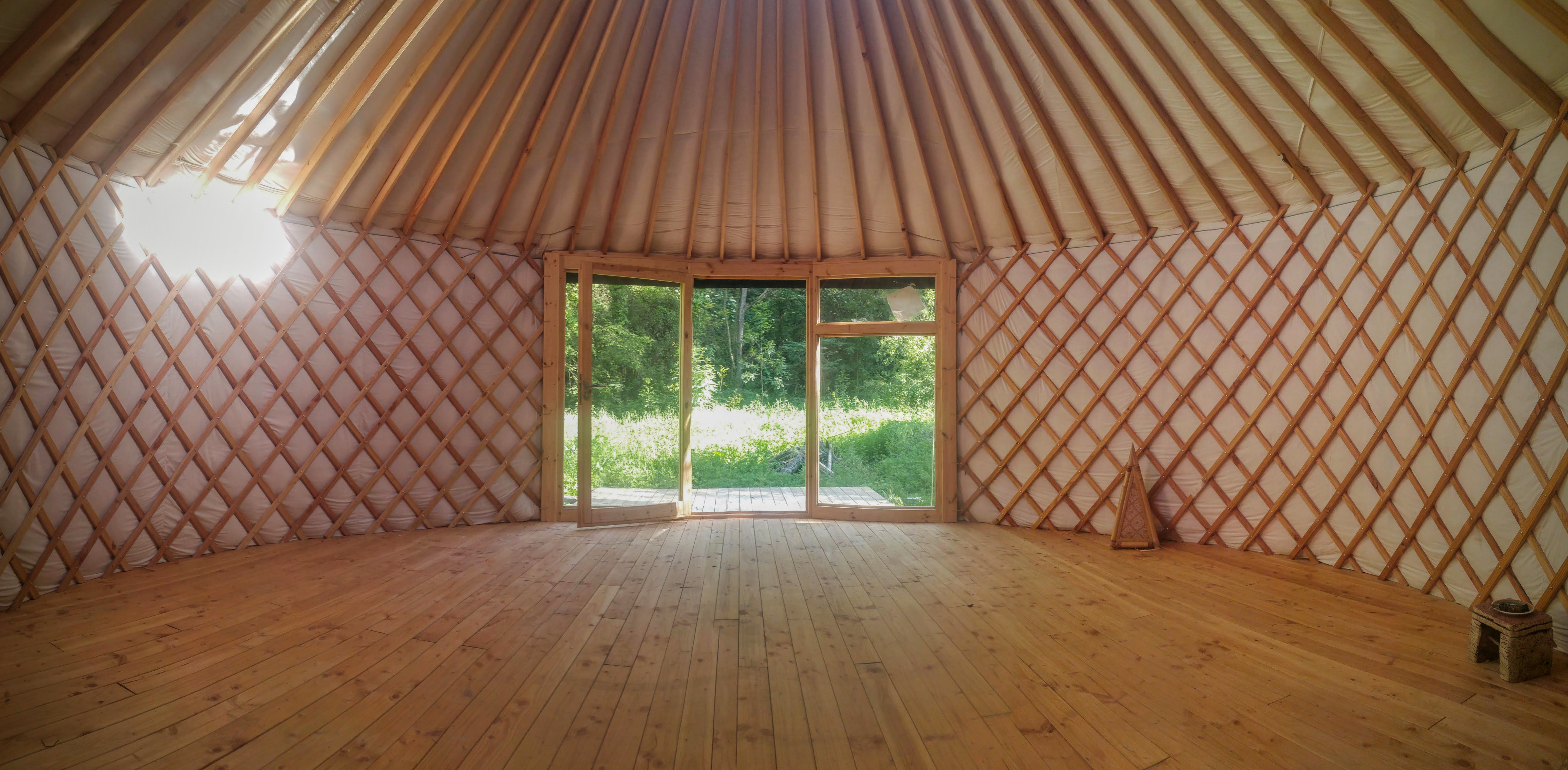 Interior amplio de yurta moderna con suelo de madera y ventana grande al jardín